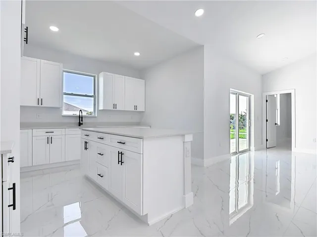 Kitchen with healthy amount of natural light, white cabinets, recessed lighting, light marble finish flooring, and light stone countertops