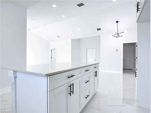 Kitchen featuring light marble finish floors, a kitchen island, white cabinetry, light stone countertops, and recessed lighting