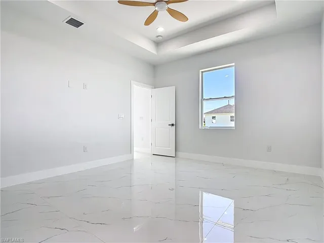 Spare room with light marble finish flooring, a ceiling fan, and a tray ceiling