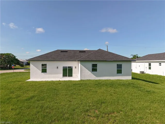 Rear view of property with stucco siding, a yard, and a shingled roof