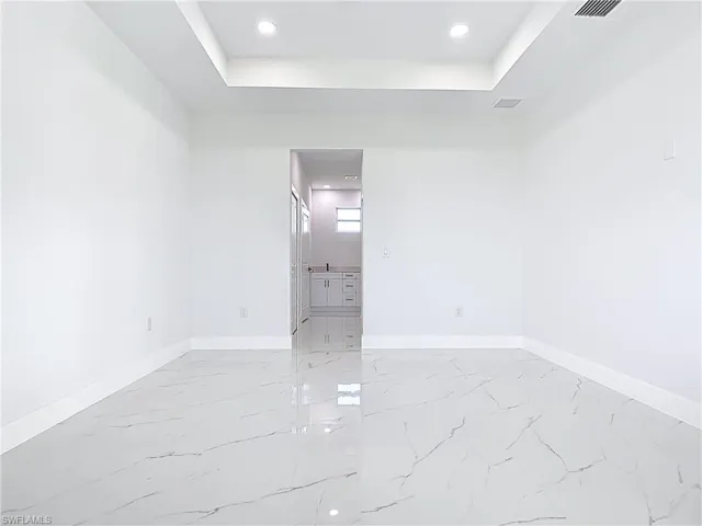 Empty room with a tray ceiling, recessed lighting, and light marble finish flooring