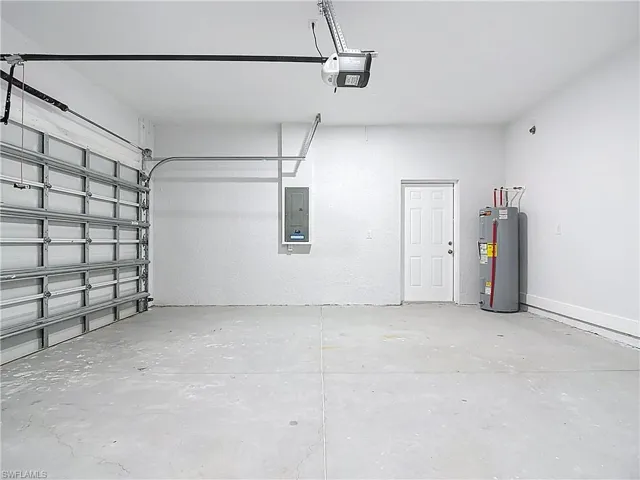 Garage with electric water heater, electric panel, and a garage door opener