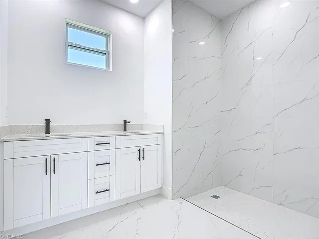 Bathroom with double vanity, a marble finish shower, light marble finish flooring, and recessed lighting