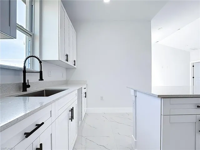Kitchen with white cabinets, light stone counters, and light marble finish flooring