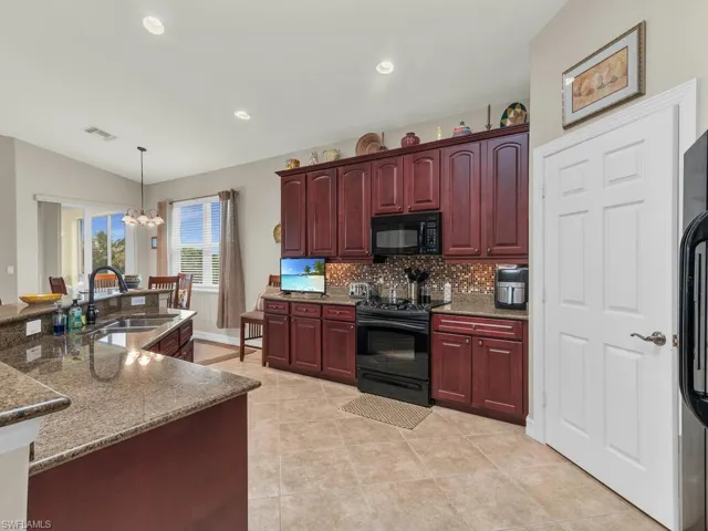 Kitchen featuring sink, black appliances, tasteful backsplash, decorative light fixtures, and lofted ceiling