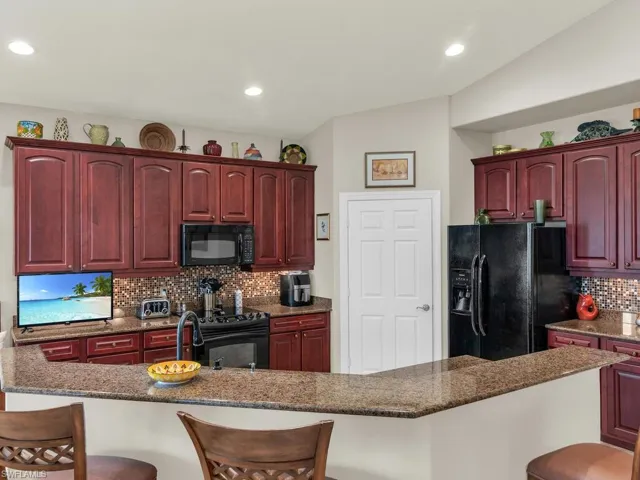 Kitchen featuring black appliances, a breakfast bar area, a kitchen island with sink, backsplash, and dark stone countertops