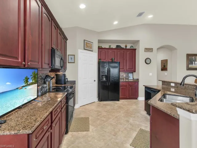 Kitchen with vaulted ceiling, decorative backsplash, black appliances, sink, and dark stone countertops