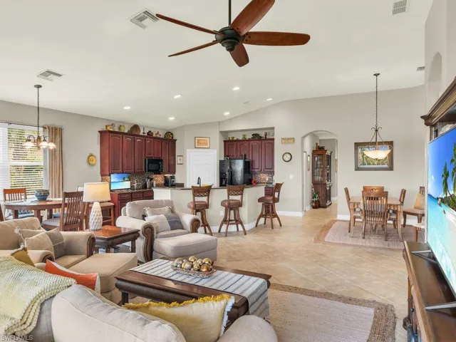 Living room with vaulted ceiling, light tile patterned floors, and ceiling fan with notable chandelier