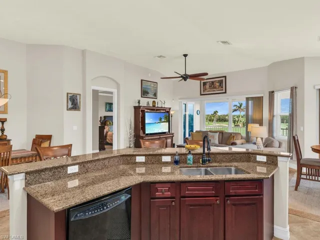 Kitchen with light stone counters, a center island with sink, black dishwasher, sink, and ceiling fan