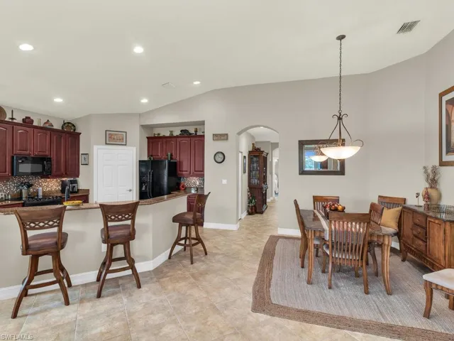 Kitchen featuring light tile patterned flooring, a breakfast bar, black appliances, tasteful backsplash, and lofted ceiling