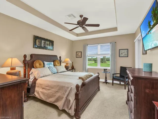Bedroom with light colored carpet, ceiling fan, and a raised ceiling