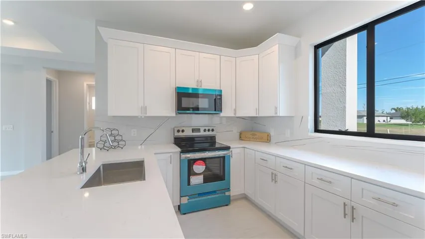 Kitchen with sink, white cabinets, electric range, and tasteful backsplash