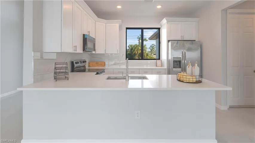 Kitchen featuring kitchen peninsula, appliances with stainless steel finishes, white cabinetry, and sink