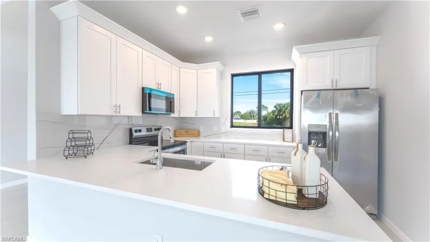 Kitchen featuring appliances with stainless steel finishes, kitchen peninsula, white cabinets, backsplash, and sink