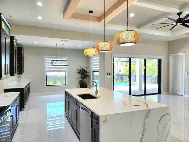 Kitchen with light stone countertops, dark cabinets, hanging light fixtures, an island with sink, and recessed lighting