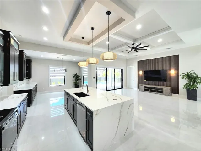 Kitchen featuring dark cabinetry, open floor plan, light stone countertops, a large island with sink, and pendant lighting