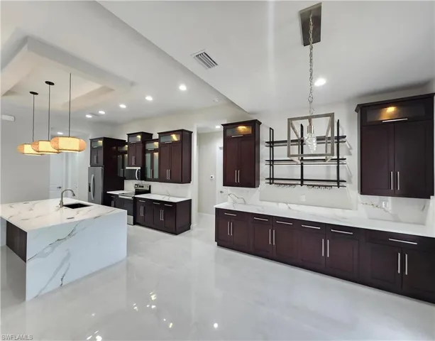 Kitchen featuring decorative light fixtures, glass insert cabinets, appliances with stainless steel finishes, dark brown cabinetry, and light stone countertops