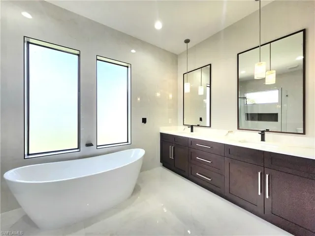 Full bathroom with a soaking tub, double vanity, light marble finish floors, and recessed lighting