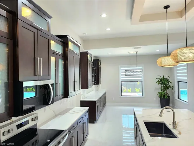 Kitchen featuring stainless steel appliances, light stone counters, hanging light fixtures, recessed lighting, and dark brown cabinetry