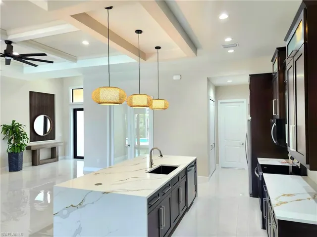 Kitchen featuring hanging light fixtures, light stone countertops, beam ceiling, a center island with sink, and recessed lighting
