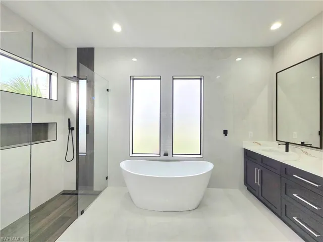 Bathroom featuring vanity, a freestanding bath, walk in shower, recessed lighting, and tile walls