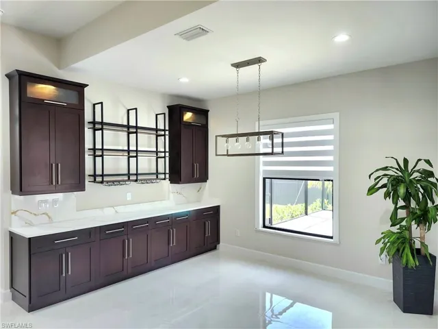 Kitchen featuring glass insert cabinets, dark brown cabinets, hanging light fixtures, recessed lighting, and light stone counters