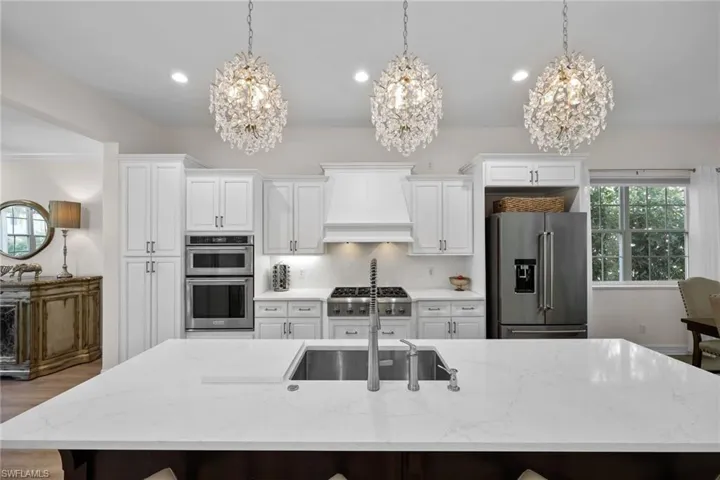 Kitchen featuring stainless steel appliances, a chandelier, a large island, wall chimney range hood, and recessed lighting