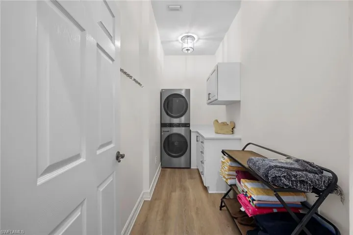 Washroom featuring stacked washer and clothes dryer, light wood-style flooring, and baseboards