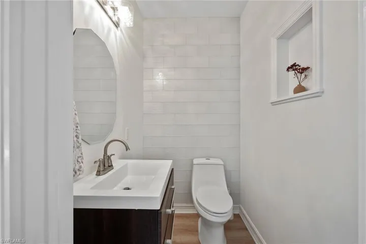 Bathroom with wood finished floors, toilet, vanity, and tile walls
