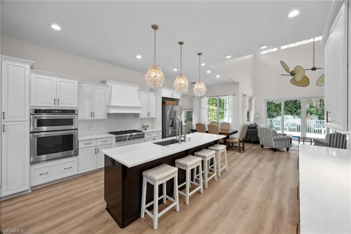 Kitchen featuring a sink, custom exhaust hood, a kitchen breakfast bar, light countertops, and white cabinetry