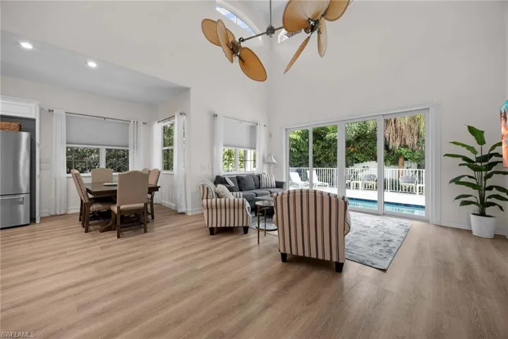 Living room with light wood-style flooring, a towering ceiling, baseboards, a ceiling fan, and recessed lighting