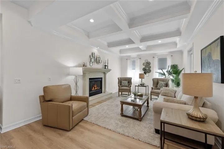 Living room featuring a glass covered fireplace, beam ceiling, light wood finished floors, coffered ceiling, and crown molding