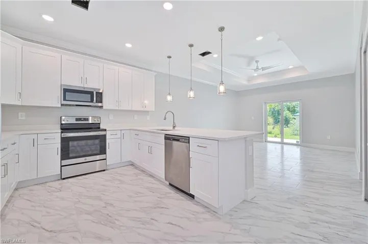 Kitchen featuring light tile flooring, kitchen peninsula, a raised ceiling, and stainless steel appliances