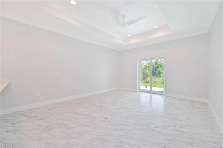 Tiled empty room featuring a tray ceiling, ornamental molding, and ceiling fan