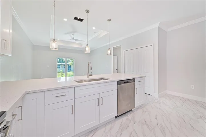 Kitchen featuring decorative light fixtures, a raised ceiling, light stone countertops, stainless steel dishwasher, and white cabinets