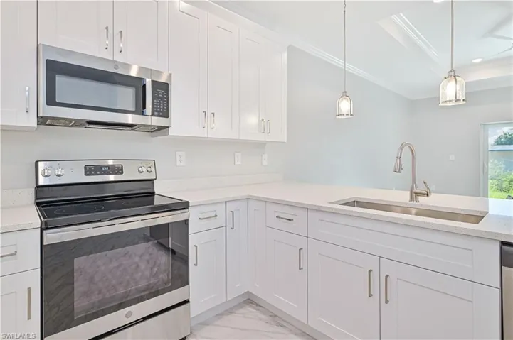 Kitchen featuring stainless steel appliances, decorative light fixtures, sink, white cabinets, and ornamental molding