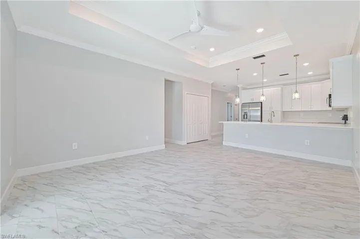 Unfurnished living room featuring light tile flooring, ceiling fan, a raised ceiling, crown molding, and sink