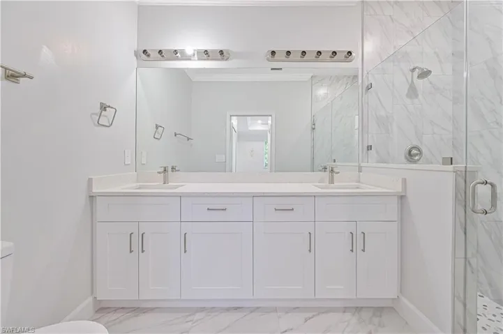 Bathroom with tile floors, an enclosed shower, vanity with extensive cabinet space, toilet, and dual sinks