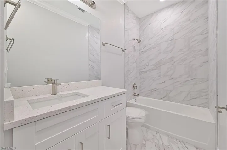 Full bathroom with tile floors, tiled shower / bath combo, vanity, and toilet