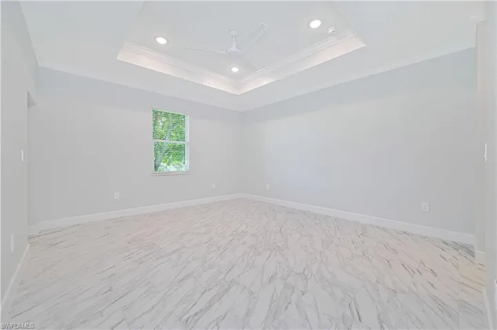 Tiled empty room featuring ceiling fan, a raised ceiling, and crown molding