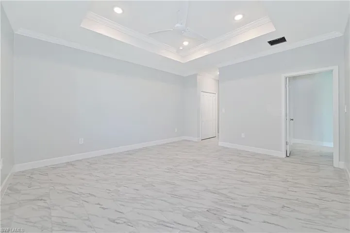Empty room with a tray ceiling, ornamental molding, and light tile flooring
