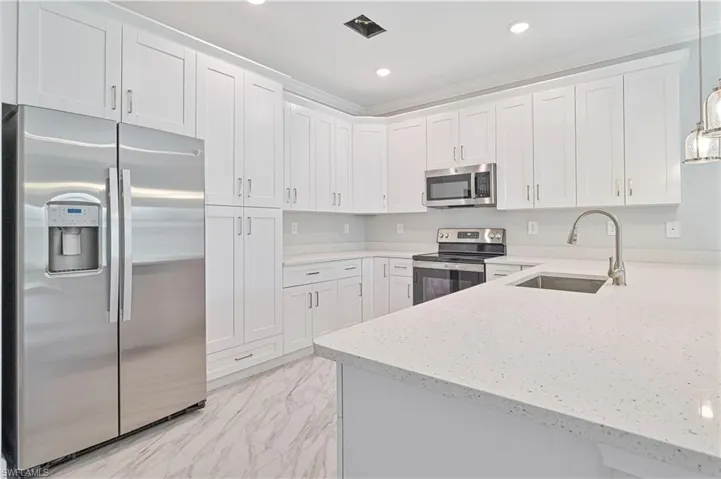 Kitchen featuring light tile flooring, light stone counters, hanging light fixtures, white cabinets, and appliances with stainless steel finishes