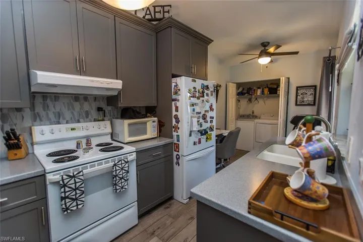 Kitchen with white appliances, gray cabinetry, washing machine and dryer, and under cabinet range hood