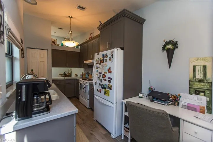 Kitchen featuring white appliances, light countertops, dark wood-type flooring, decorative light fixtures, and under cabinet range hood