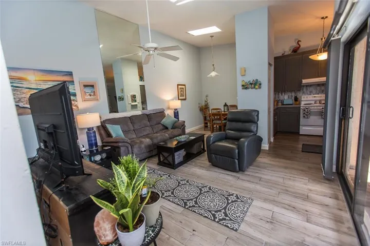 Living area with light wood-style tiles, a ceiling fan, high vaulted ceiling, and a skylight