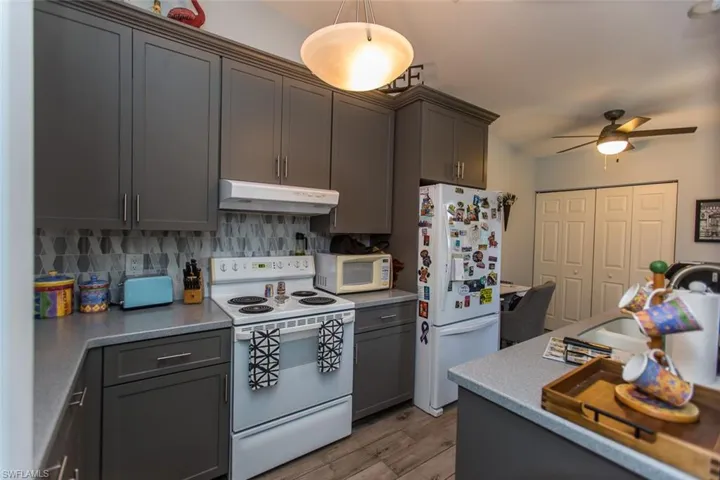 Kitchen featuring white appliances, gray 42" cabinetry, light wood-style flooring, under cabinet range hood, and backsplash