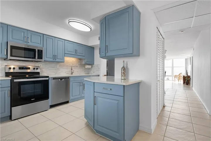 Kitchen featuring blue cabinets, appliances with stainless steel finishes, backsplash, and light tile patterned floors