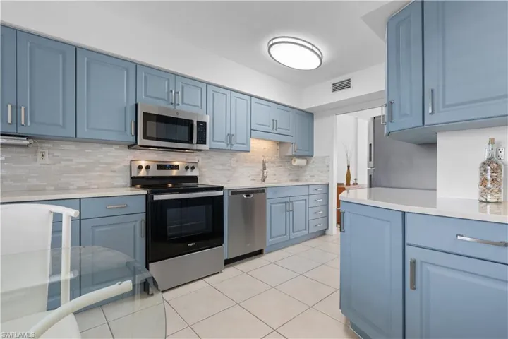 Kitchen featuring blue cabinets, appliances with stainless steel finishes, light tile patterned floors, and decorative backsplash