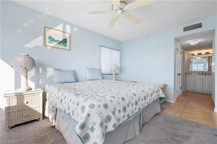 Bedroom featuring ensuite bath, ceiling fan, light tile patterned floors, and a textured ceiling