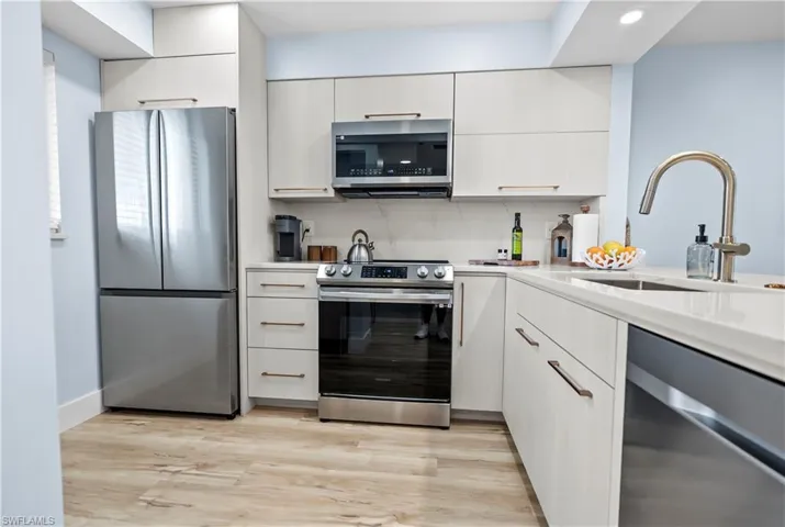 Kitchen featuring light wood-style flooring, light countertops, white cabinetry, stainless steel appliances, and a sink